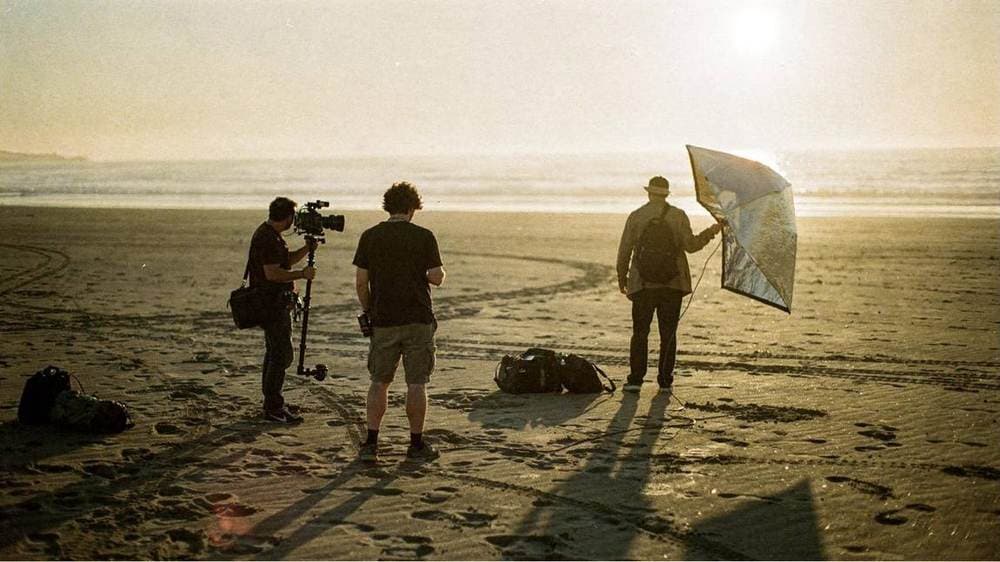 A small film crew setting up a shot on a winter beach at dawn, generated in Omnibo
