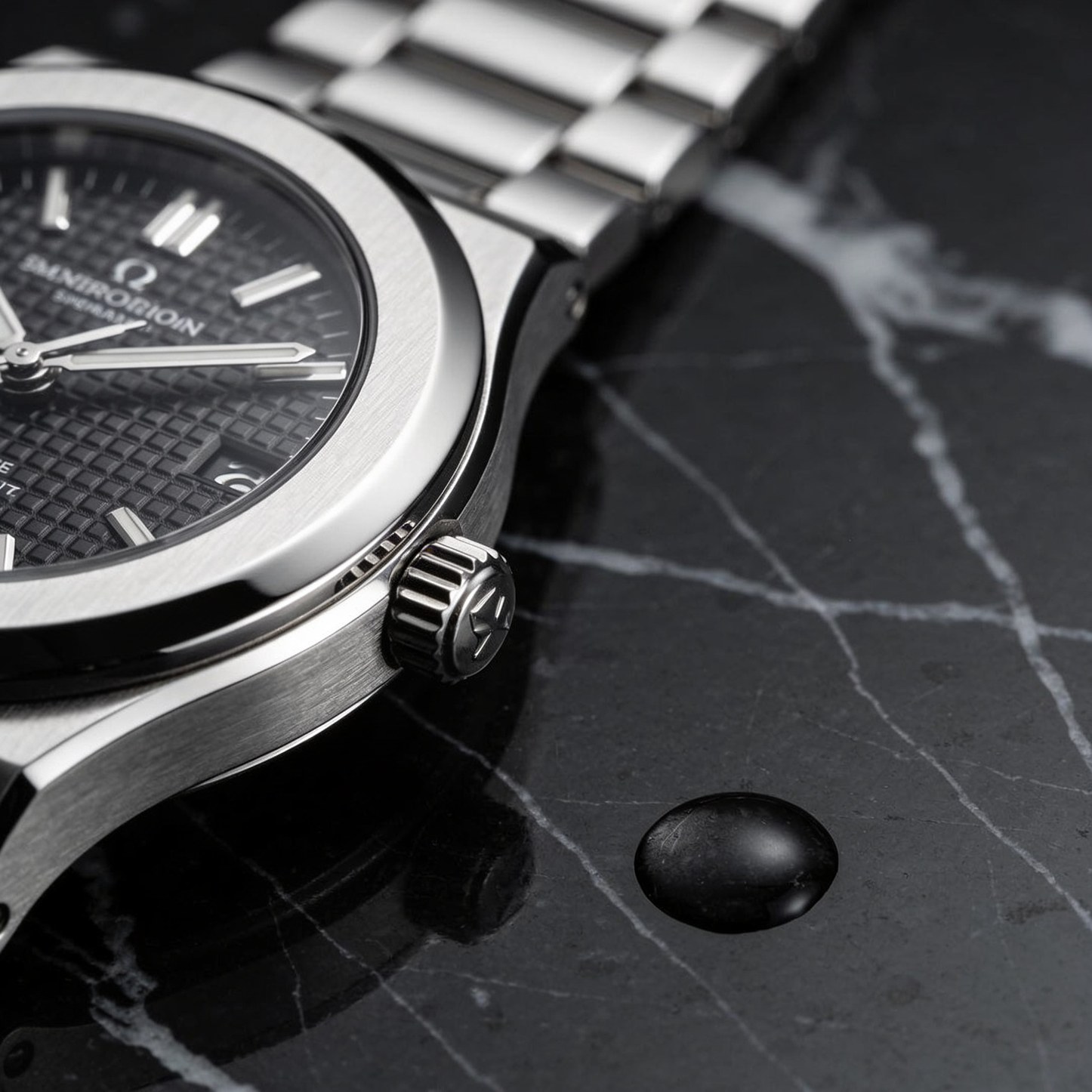 A steel wristwatch on veined black marble beside a single water droplet